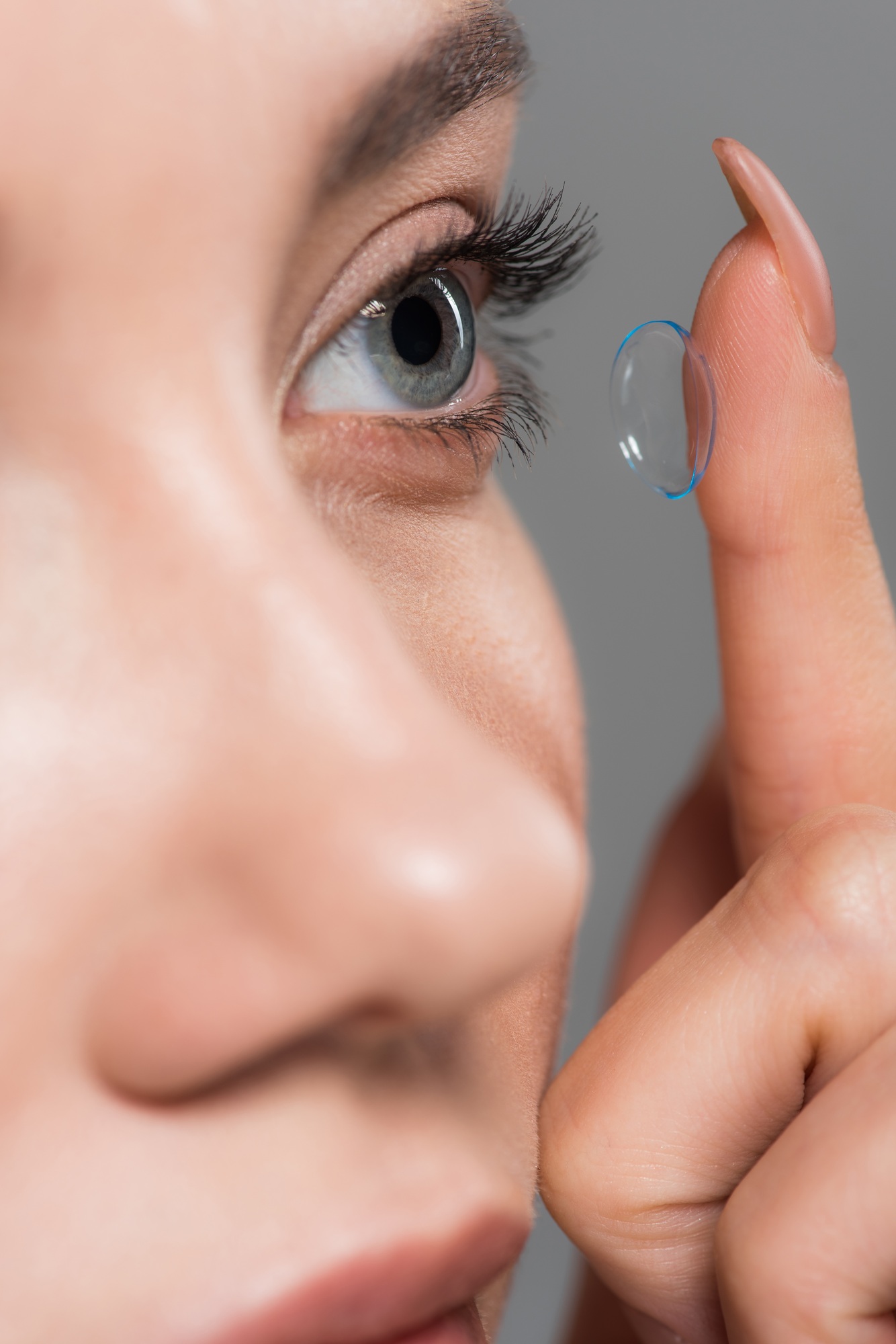 selective focus of young woman attaching contact lens isolated on grey